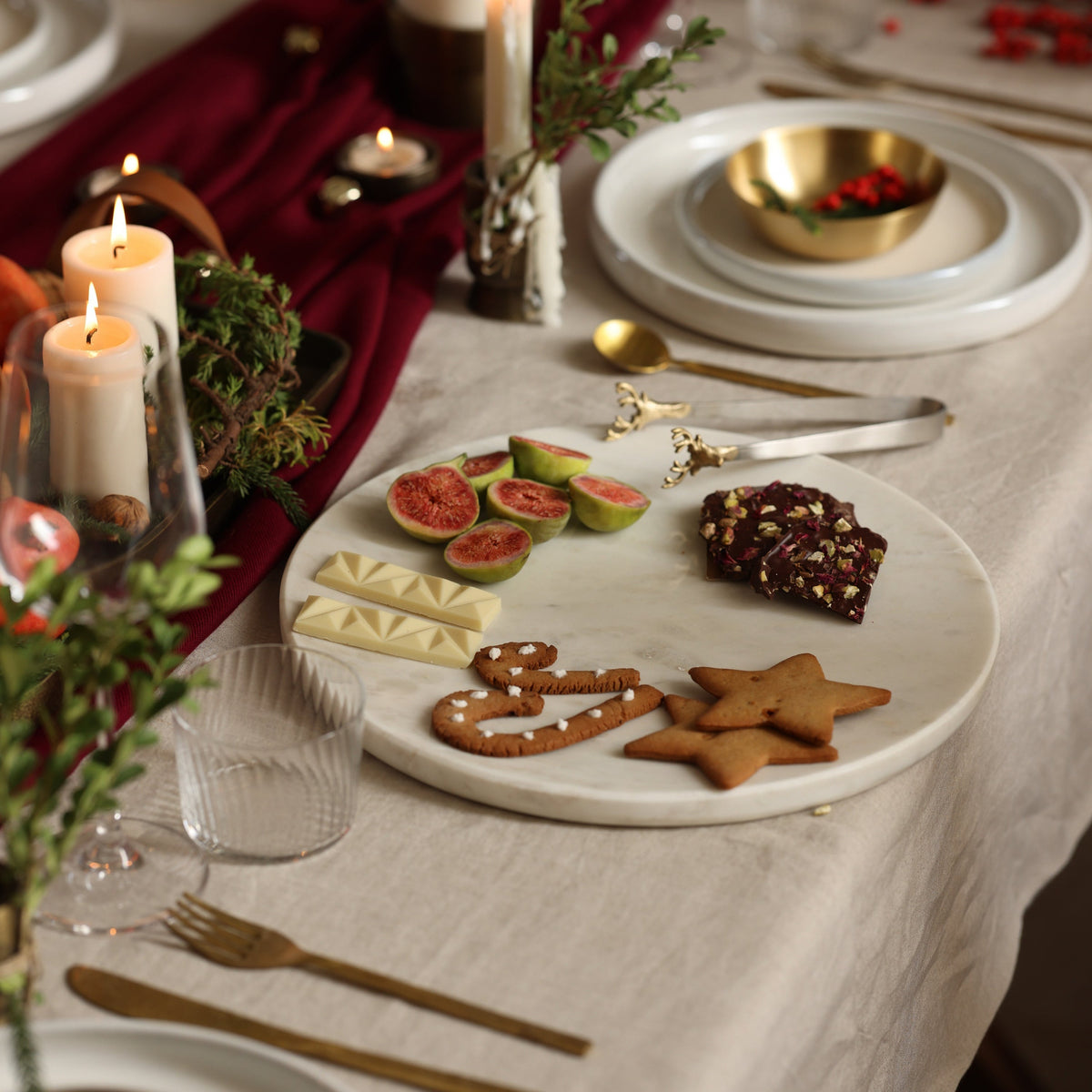 White marble platter on a laid table with figs, chocolate and biscuits
