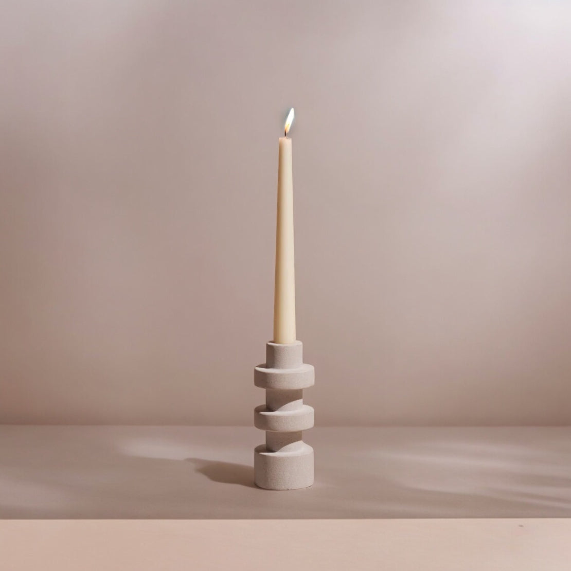 Tall Pilar Tear candle holder in pale sandstone, stacked offset tiers, holding a lit ivory taper