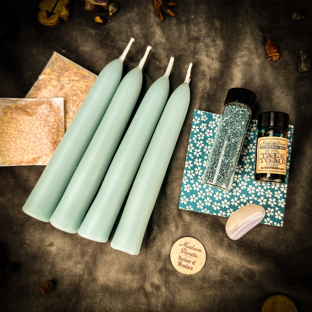 The same Communication pack on dark gray cloth under warm light, which reads the pale blue tapers a soft mint; dried leaves lie around the edge.