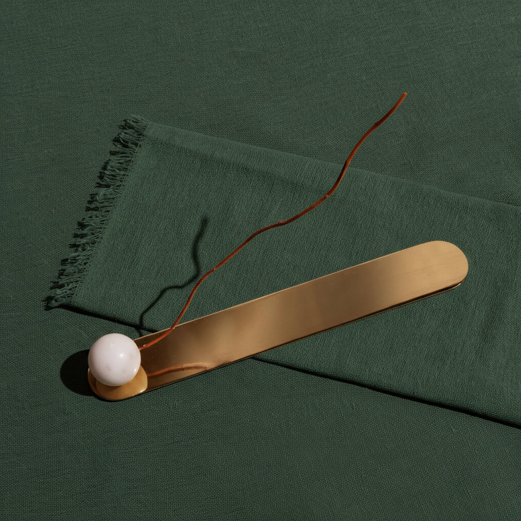 Anka brass incense holder with a white marble sphere, an incense stick resting in it, on green linen