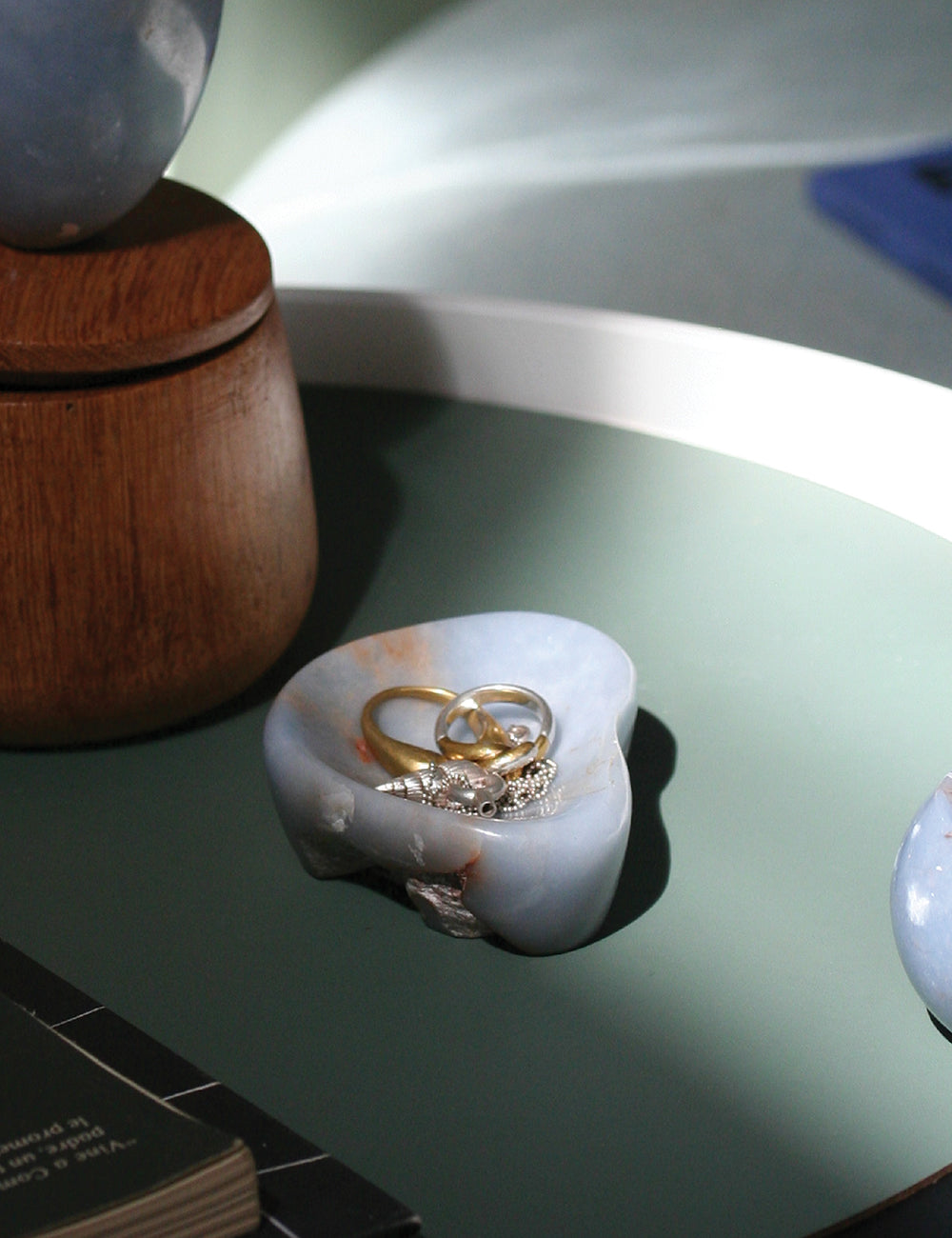 Blue angelite catchall with rings on a green tabletop beside a wooden box