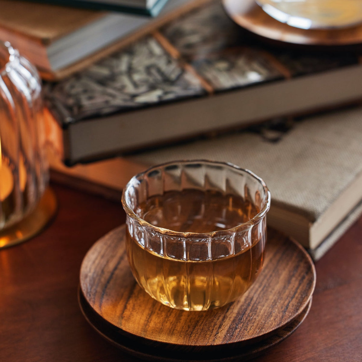Single Kira glass cup on a wooden coaster beside old books