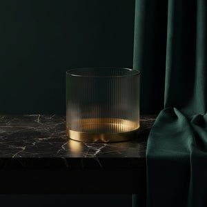 Fluted glass vase with a brass base on dark marble against green velvet