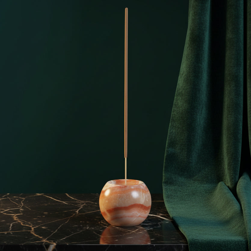 Cream onyx sphere incense holder with peach banding on black marble, stick burning