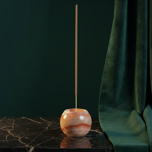 Cream onyx sphere incense holder with peach banding on black marble, stick burning