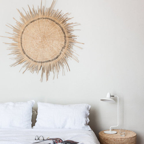 Sun Circle disc hung above a made bed with a reading lamp