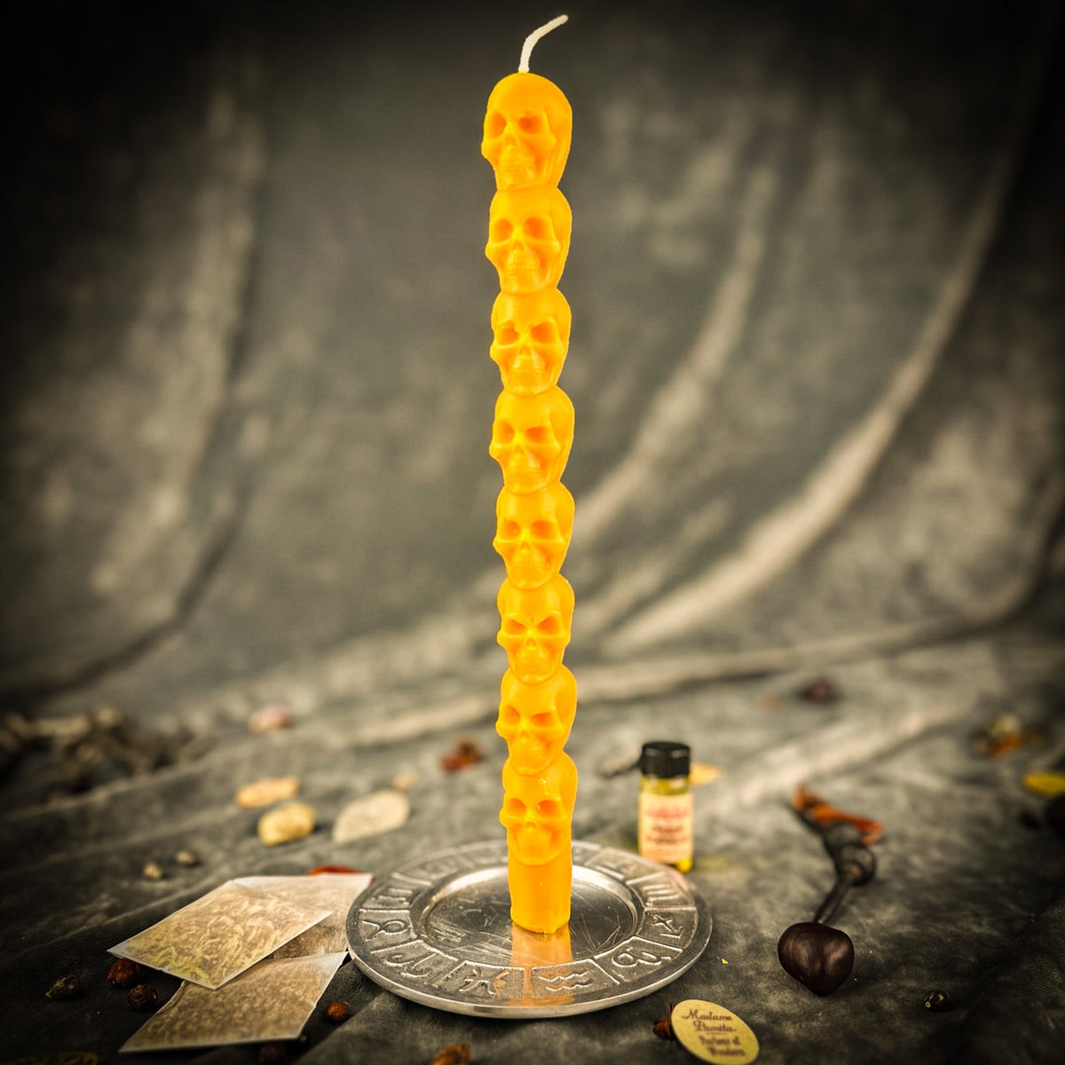 Golden yellow beeswax skull taper candle standing in a brass holder beside tarot cards and a vial of dressing oil
