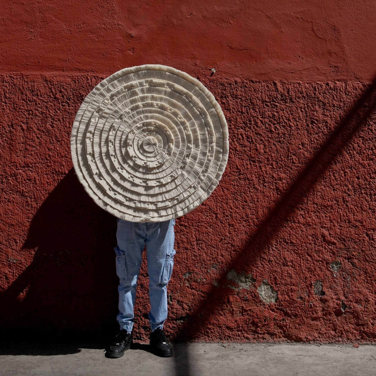 Person holding the tapestry against a deep red wall in full sun