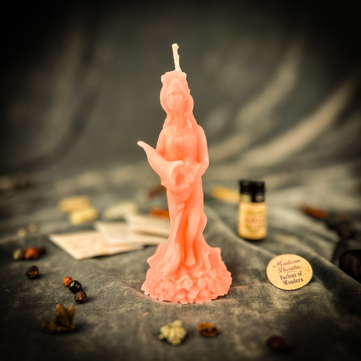 Fortuna goddess candle in coral pink with the kit components on draped gray fabric