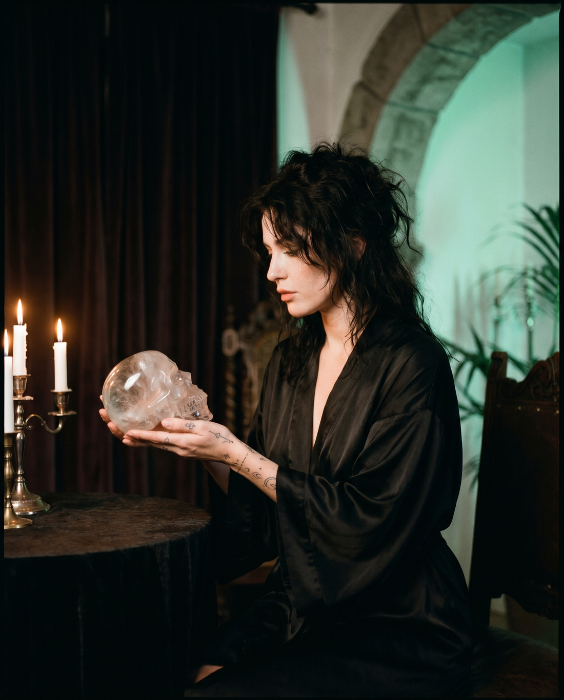Woman in a black silk kimono holding a clear quartz skull by candlelight