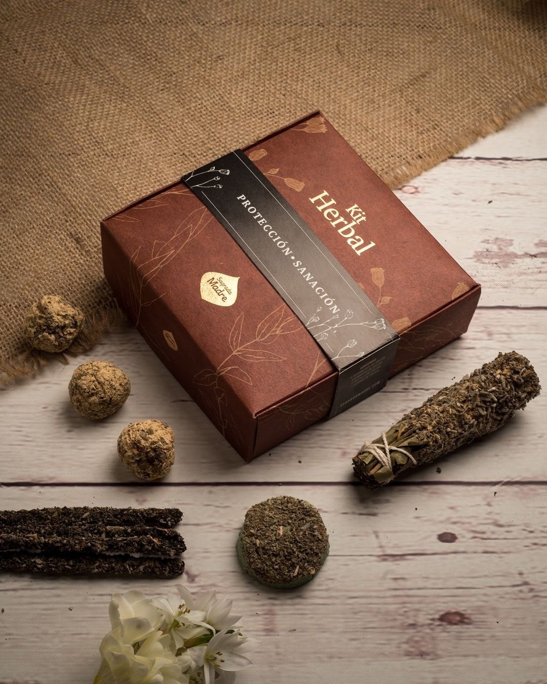 Closed Sage Herbal gift box on pale wood with a smudge stick and smudge bombs beside it