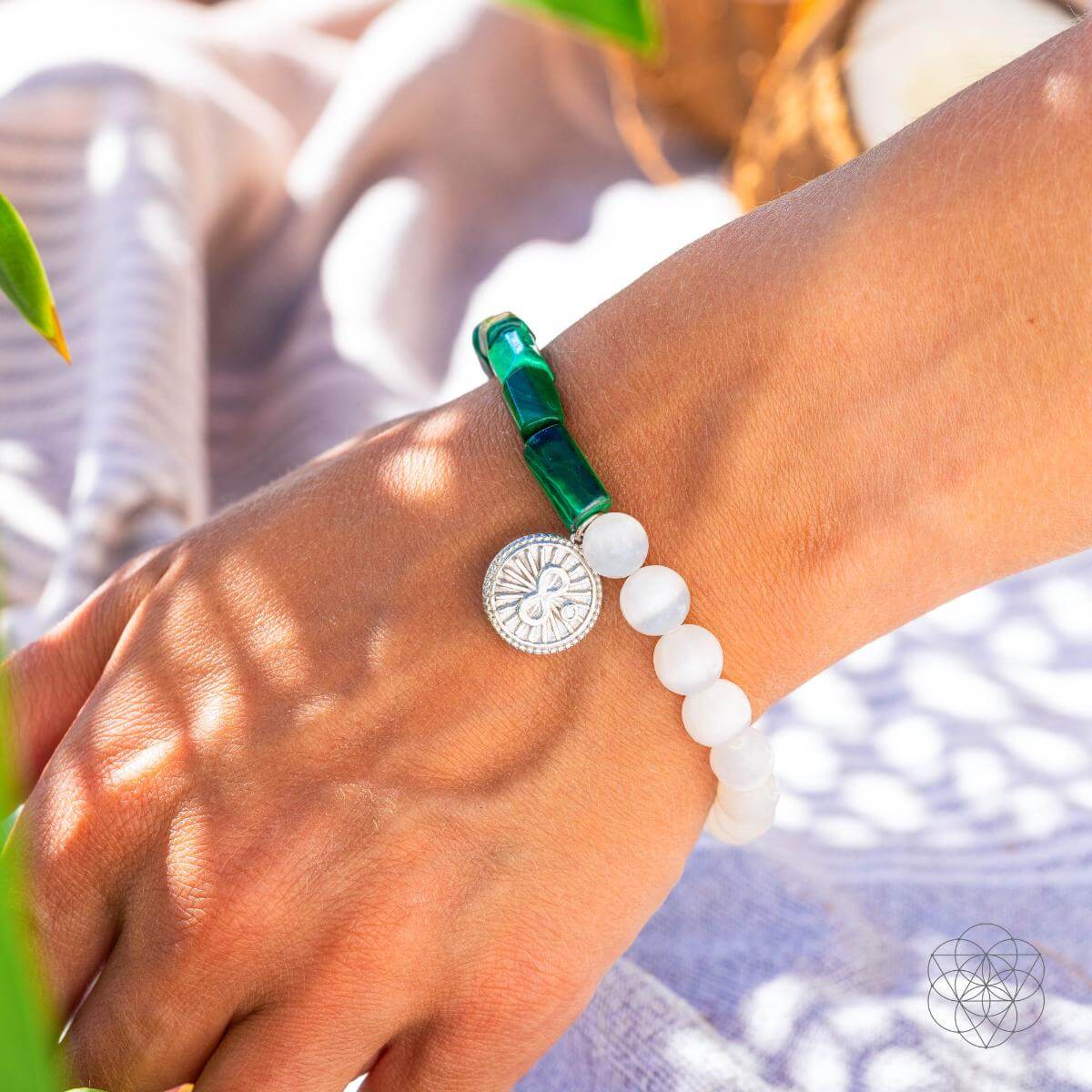 Bracelet with deep green malachite beads on one side and translucent selenite on the other, joined by a platinum-plated infinity charm — detail view 2