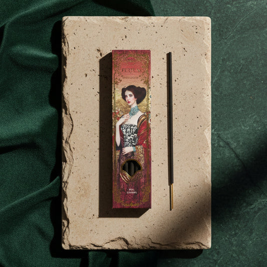 The carton and a single incense stick on a pale stone slab over dark green velvet, the box printed with an Art Nouveau woman in red and gold.