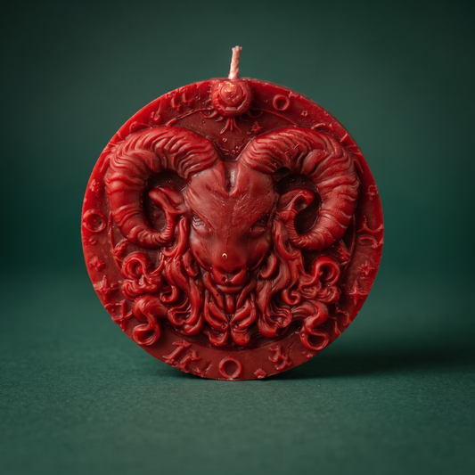 Red Aries candle against a dark green background: a round beeswax medallion on small feet, a ram's head with curled horns in high relief, planetary glyphs around the border.