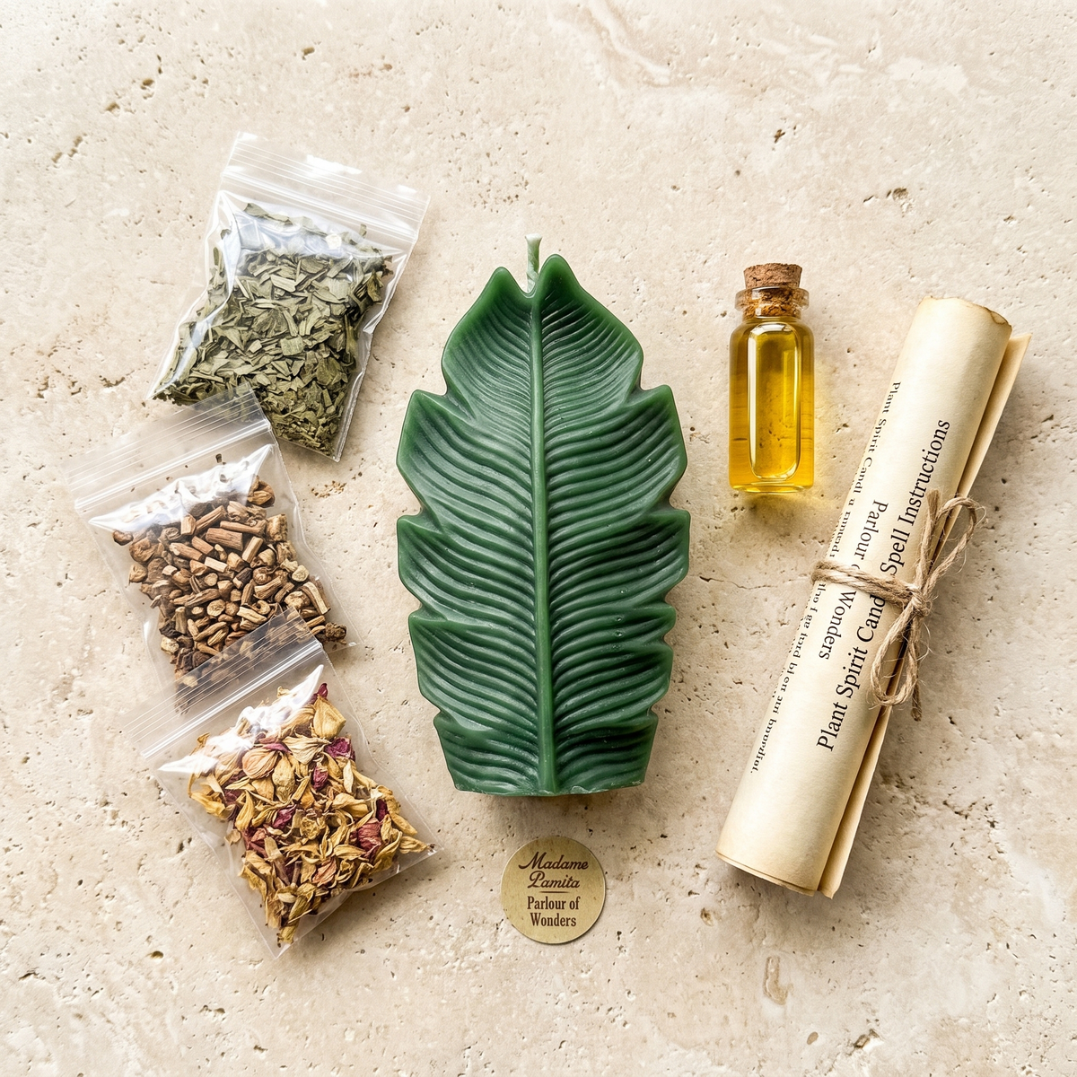 Dark green leaf-shaped spell candle laid on pale stone with three sealed bags of dried herbs, bark and rose petals, a corked vial of oil and a rolled instruction scroll tied with twine