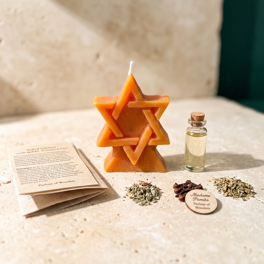 Seal of Solomon spell kit laid out on stone: an orange beeswax hexagram candle with the printed instruction sheet, a corked vial of dressing oil and three small piles of dried herbs