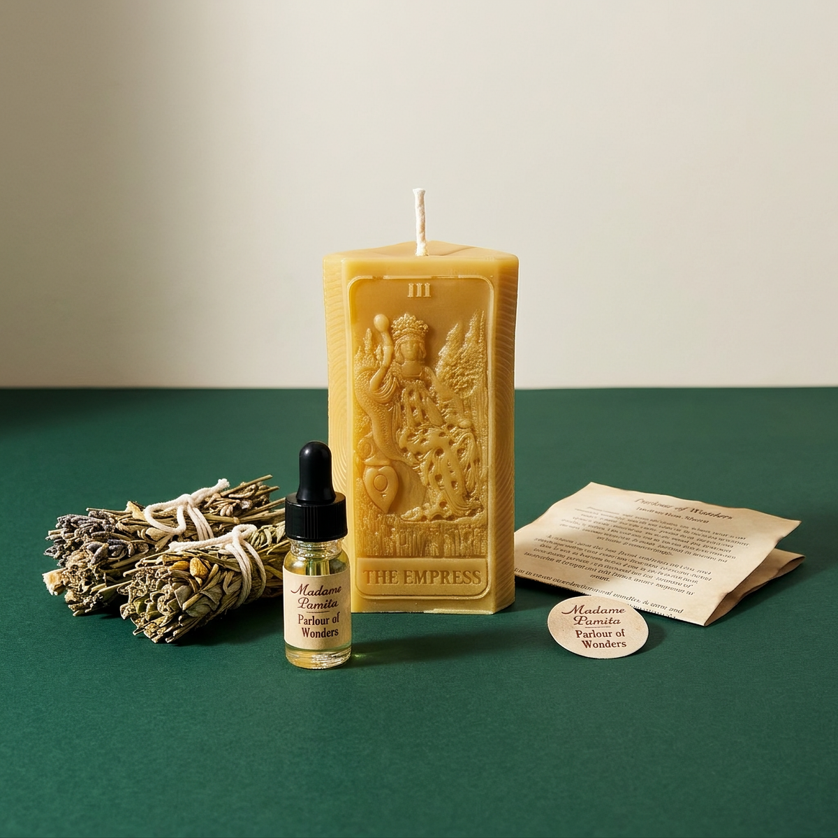 The Empress candle spell kit laid out on green: a natural beeswax tarot-card candle with a white sage bundle, a dropper bottle of dressing oil and the instruction sheet