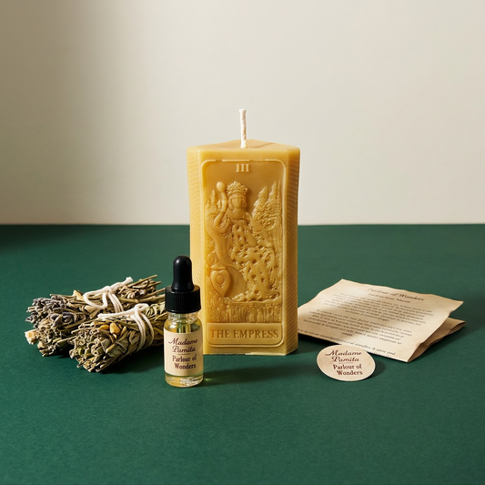 The Empress candle spell kit laid out on green: a natural beeswax tarot-card candle with a white sage bundle, a dropper bottle of dressing oil and the instruction sheet