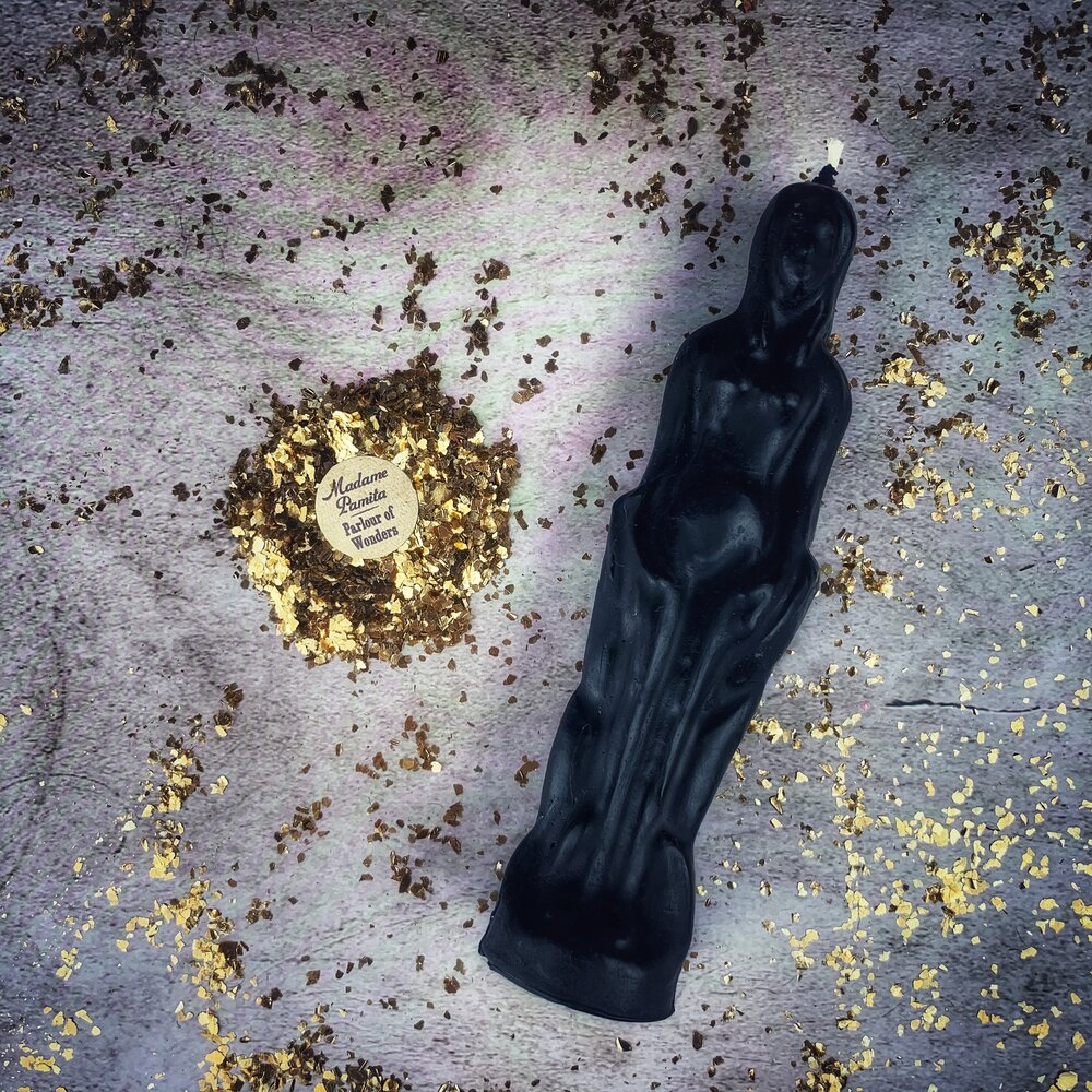 Black beeswax female figure candle on gray cloth with scattered dried botanicals