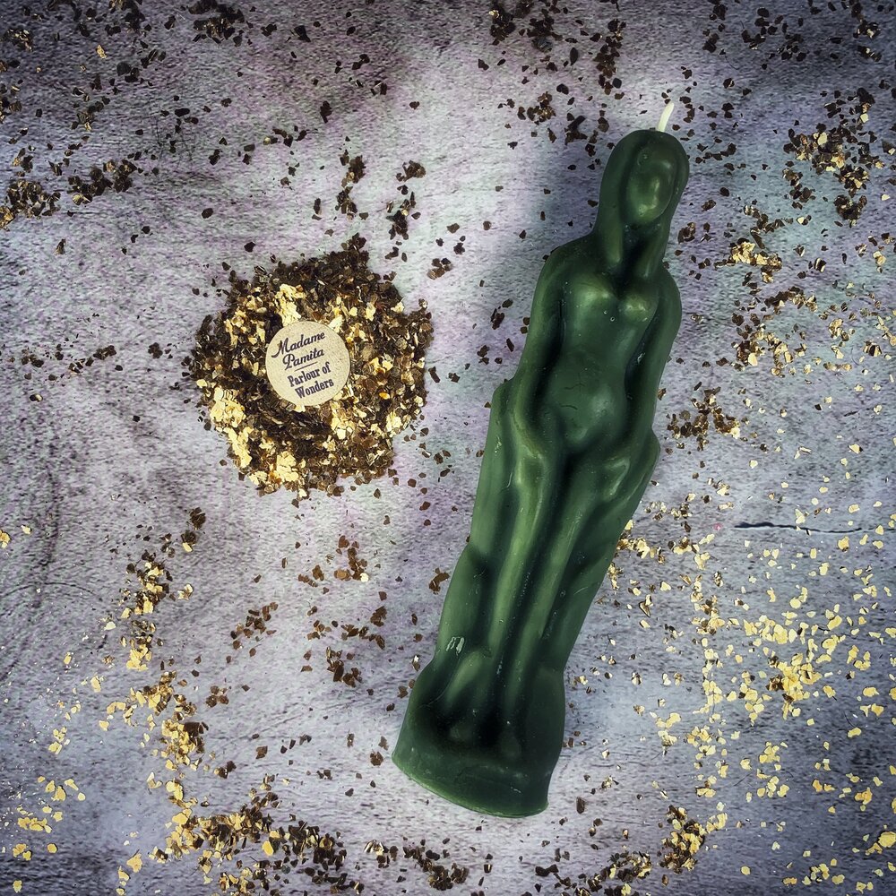 Dark green beeswax female figure candle on gray cloth with a ring of dried herbs