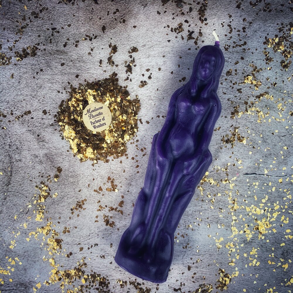 Purple beeswax female figure candle on gray cloth with gold flecks and crushed herbs