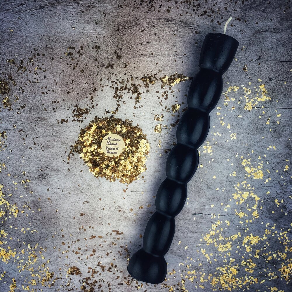 Black seven knob candle lying diagonally on gray stone with gold leaf flakes around it.