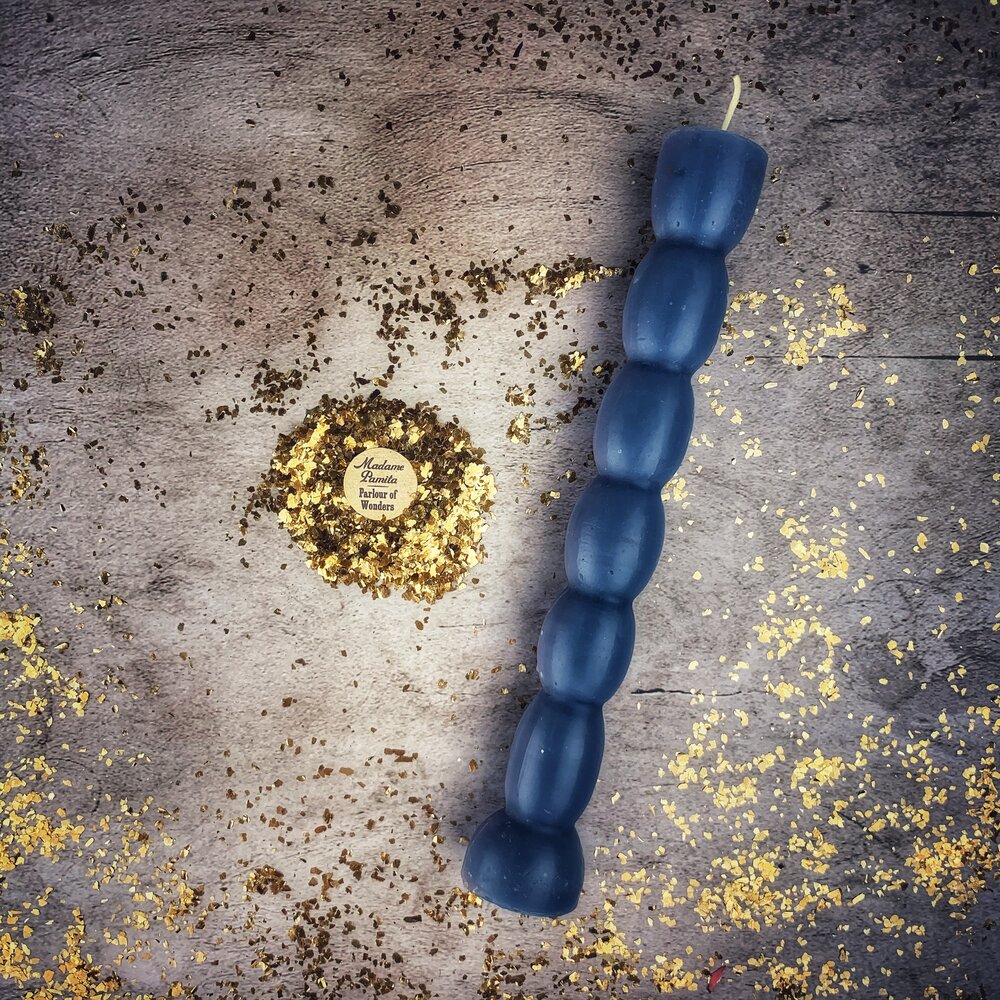 Slate-blue seven knob candle lying beside the herb-and-gold-leaf label.