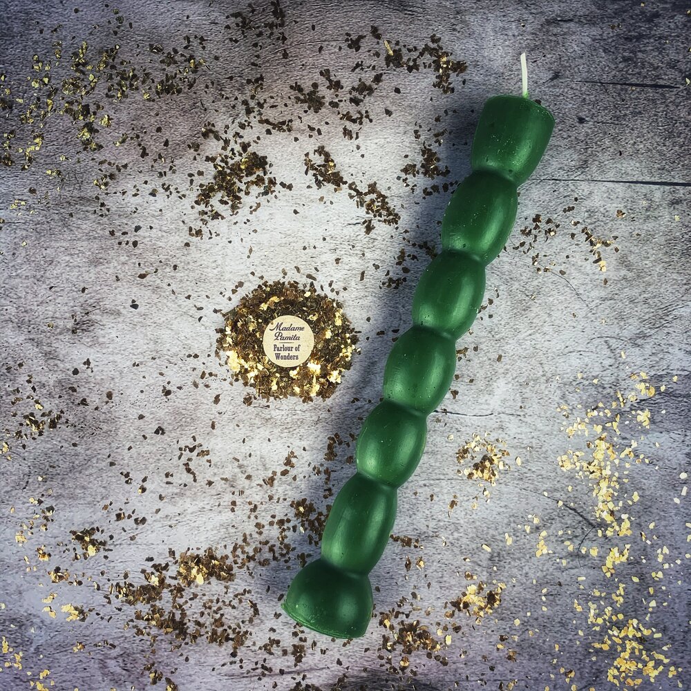 Deep green seven knob candle on gray stone, gold leaf scattered around it.
