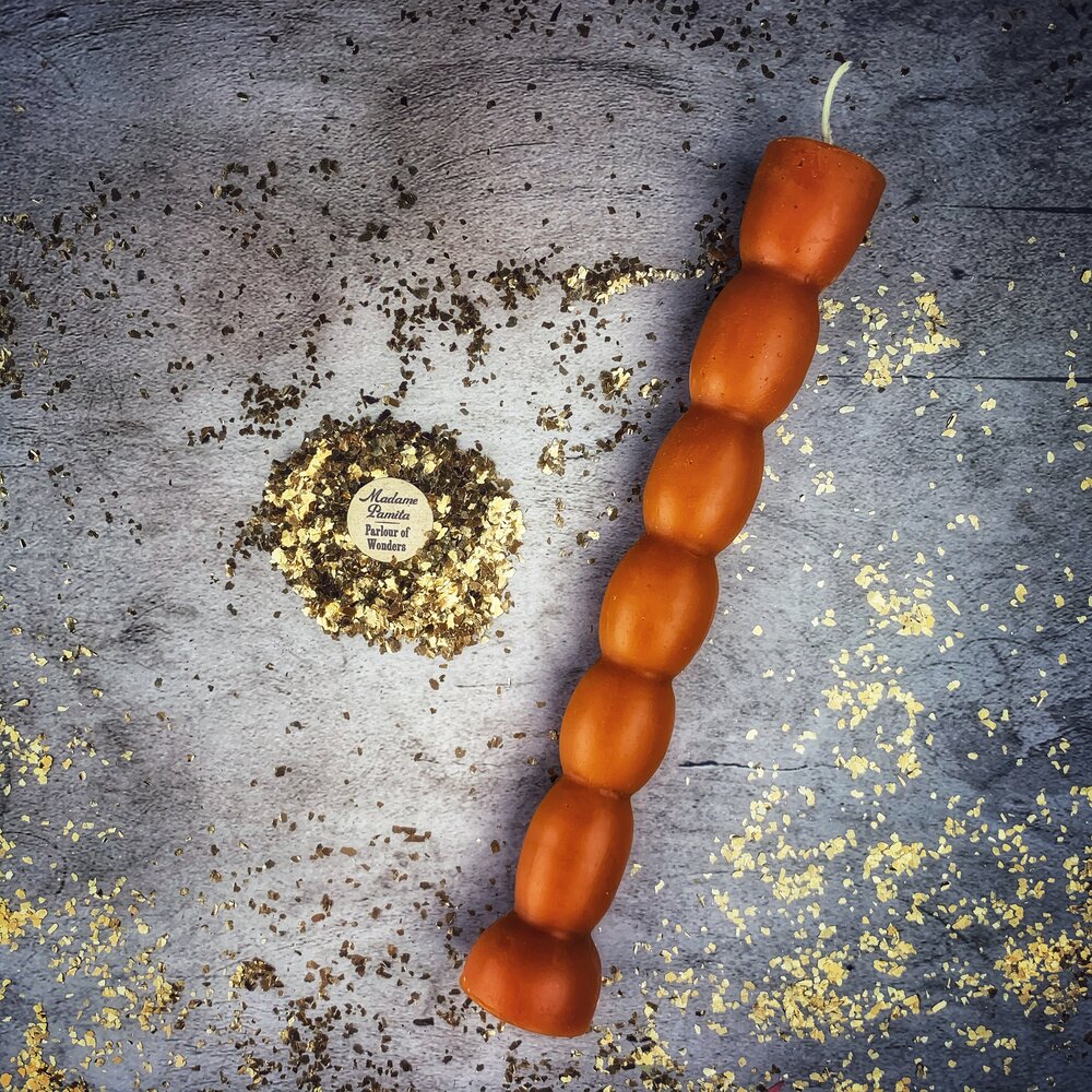 Burnt-orange seven knob candle lying on gray stone, wick uncut at the top.