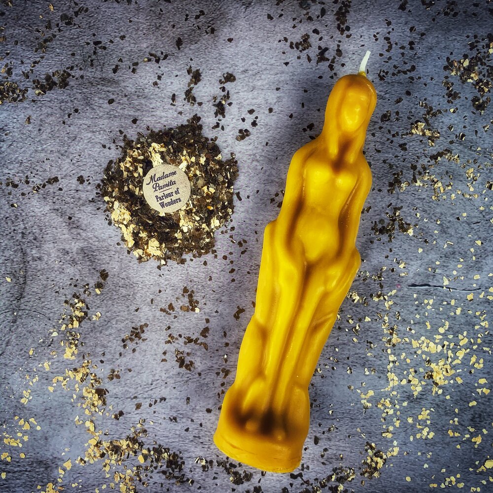 Golden yellow beeswax female figure candle on gray fabric with dried herbs