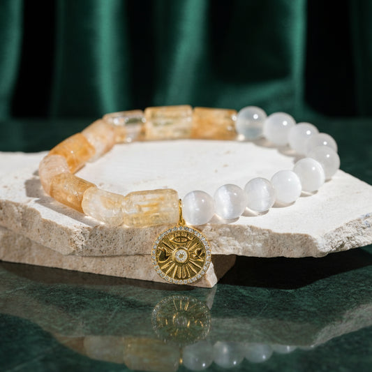 The Quartet of Luck bracelet on a pale stone slab against dark green: rectangular raw citrine beads, round selenite beads and a gold talisman charm