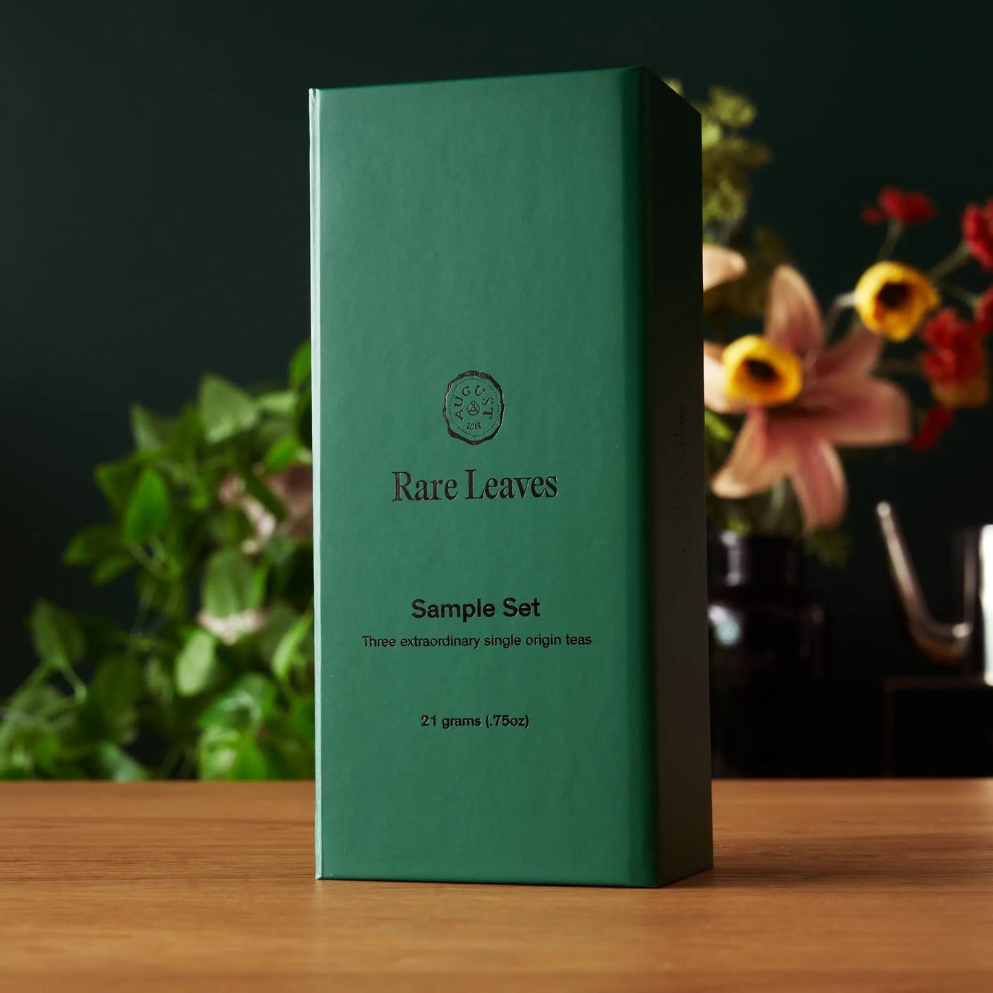 The dark green Rare Leaves sample set box, holding three single-origin tea tins, on a wooden surface.