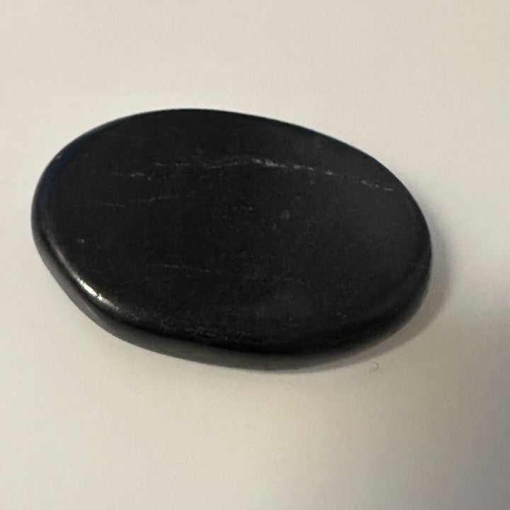Flat matte black Russian shungite palm stone held for scale