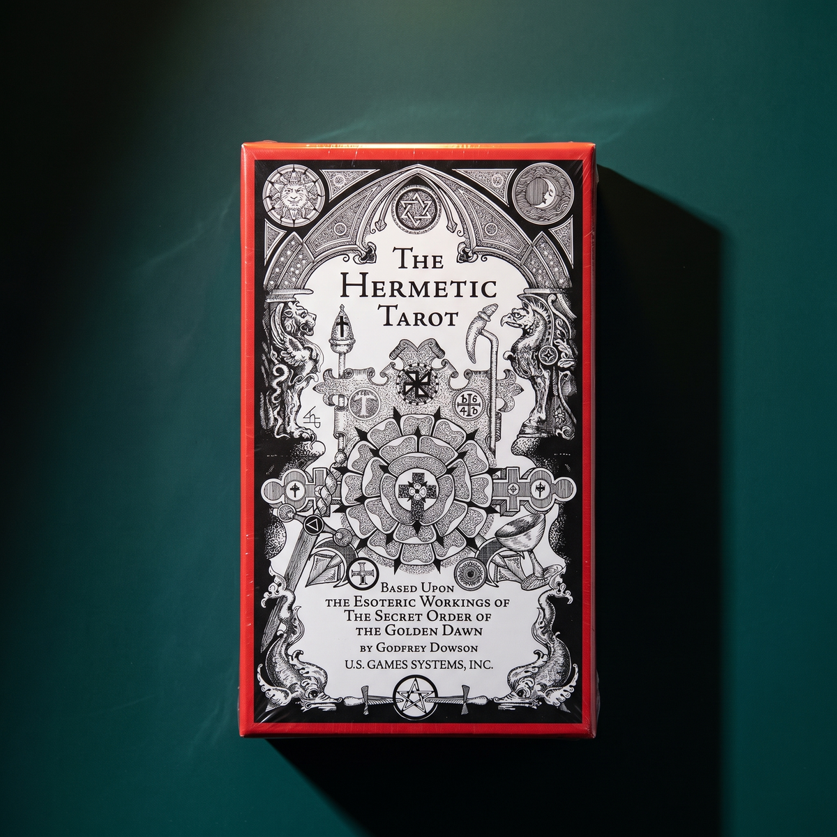 The Hermetic Tarot box standing upright on dark green velvet, its red-edged black-and-white cover lit from one side