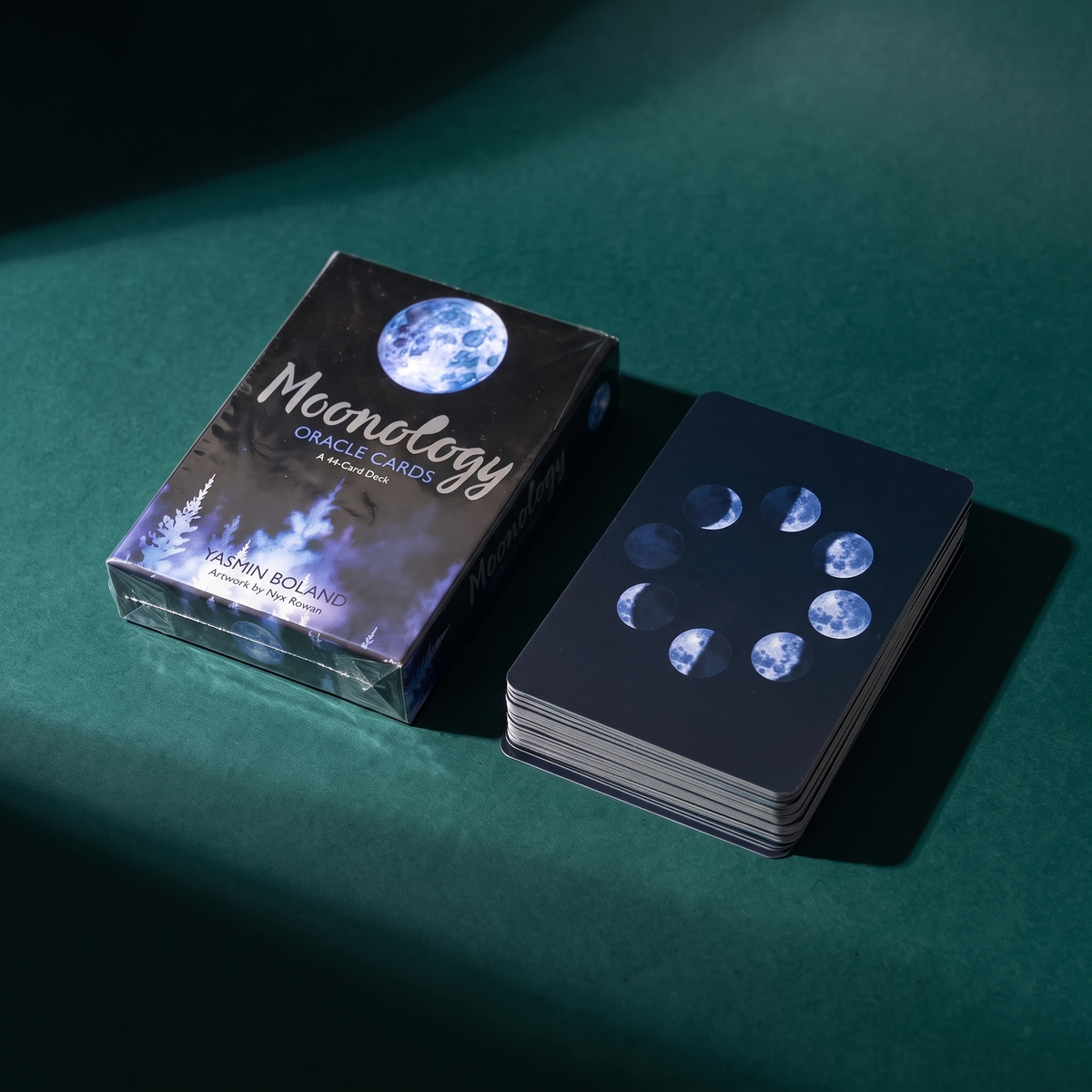 Moonology Oracle Cards box beside a face-down stack of the deck on dark green velvet, the card backs printed with moon phases