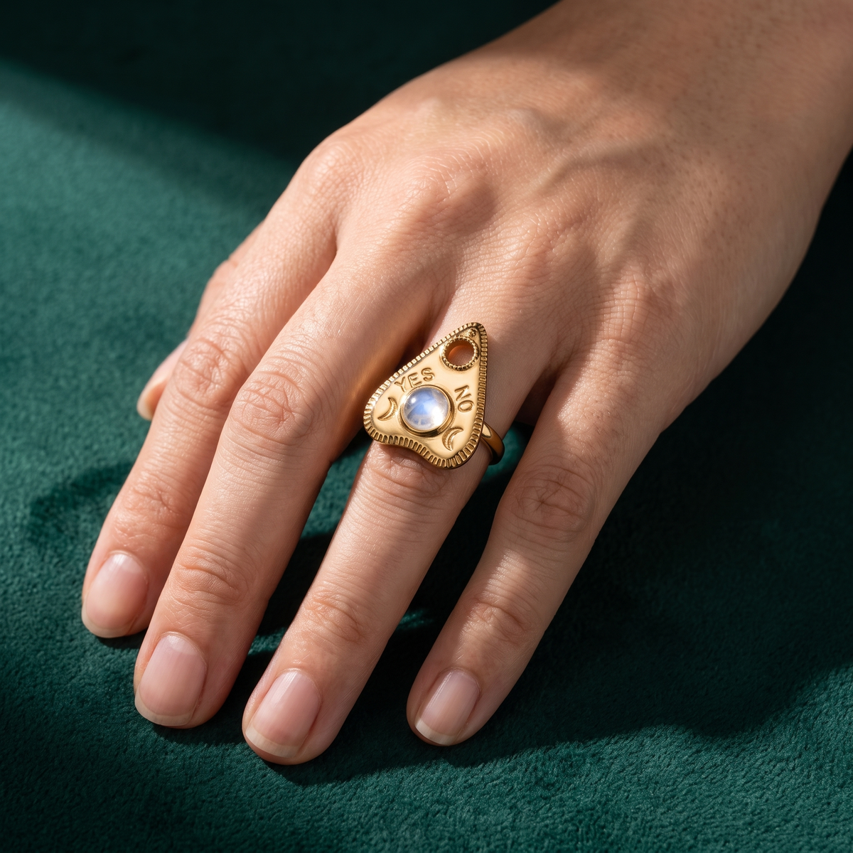 The planchette ring worn on a hand against green velvet, showing how the teardrop face sits across the finger
