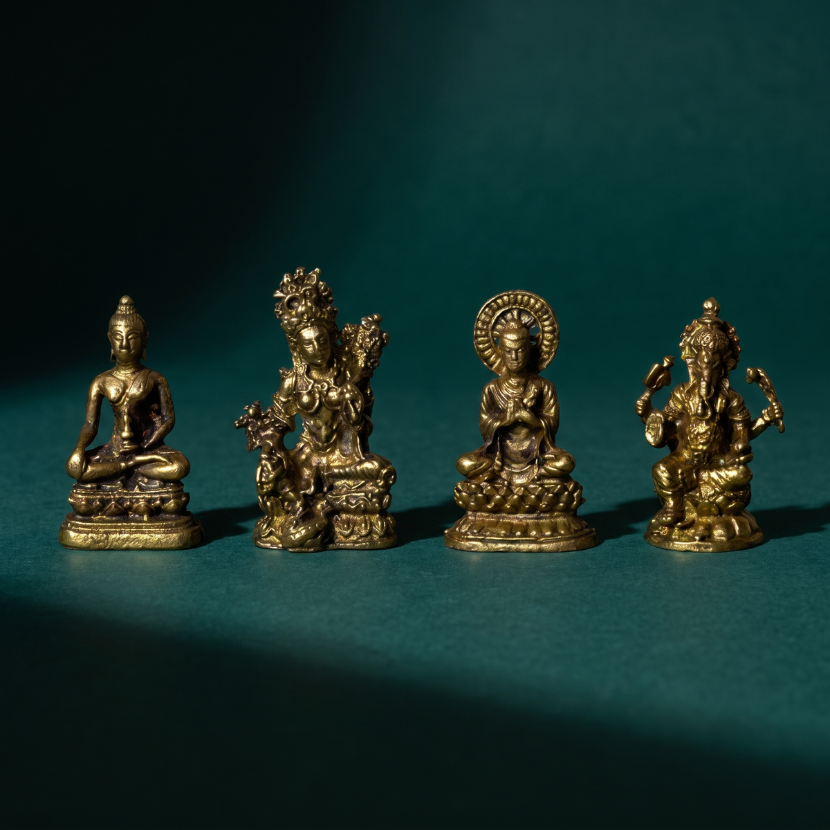 Four miniature brass altar figures standing in a row on dark green velvet, each on its own cast base
