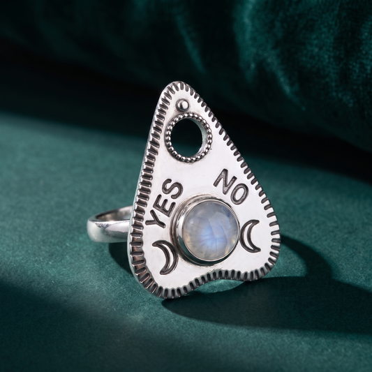 Rainbow moonstone planchette ring standing on dark green velvet, YES and NO lettering flanking the round cabochon
