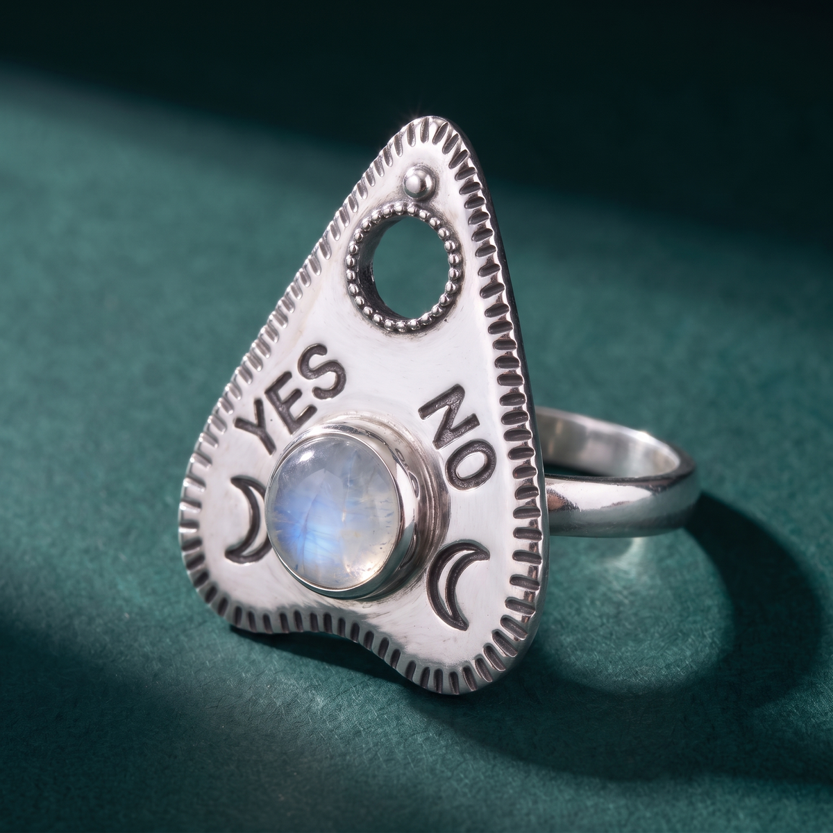 Close view of the planchette ring on green velvet, the moonstone cabochon set between the YES and NO lettering