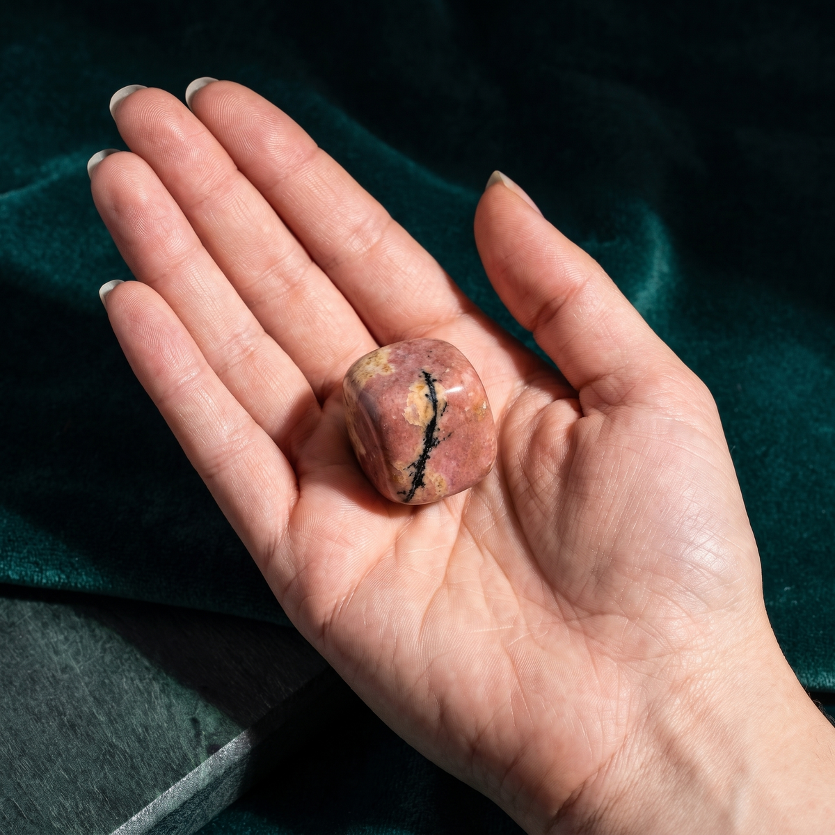 A hand holding the rhodonite pocket stone to show its size against the palm