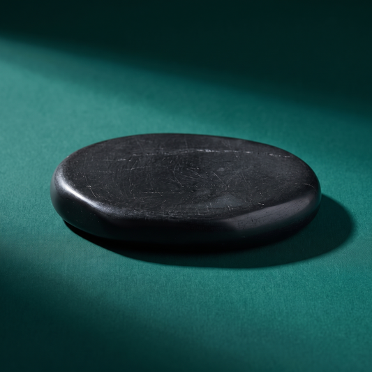 A flat black Russian shungite palm stone on a dark green surface, matte and unreflective