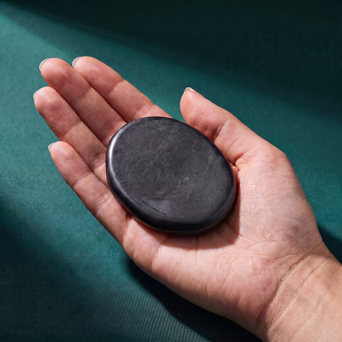 A hand holding the flat shungite palm stone, which covers most of the palm