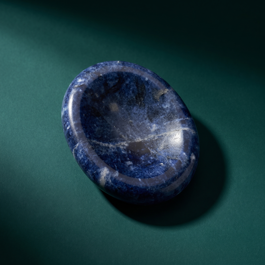 A sodalite comfort stone on dark green, its oval face dished into a shallow thumb hollow