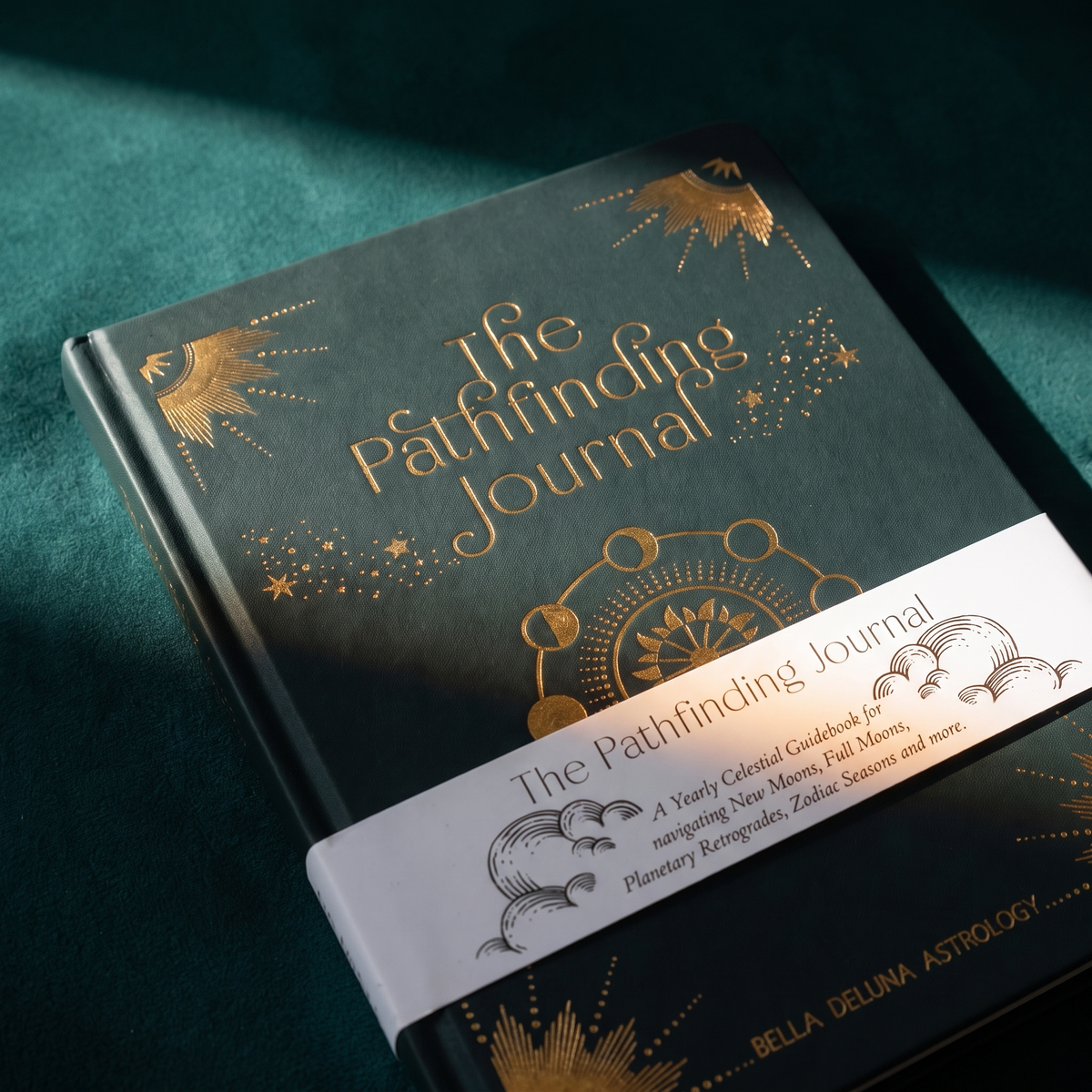 The Pathfinding Journal lying at an angle on dark green velvet, gold sunburst and moon-phase arc across the cover
