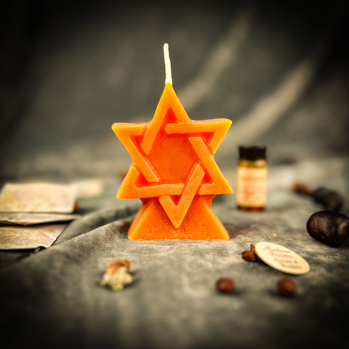 Orange beeswax Seal of Solomon hexagram candle standing on gray cloth beside a vial of dressing oil