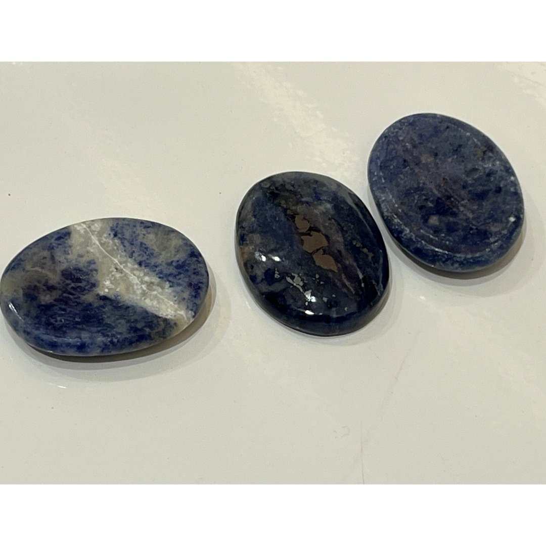 Three sodalite comfort stones side by side, showing variation in their blue and white patterning