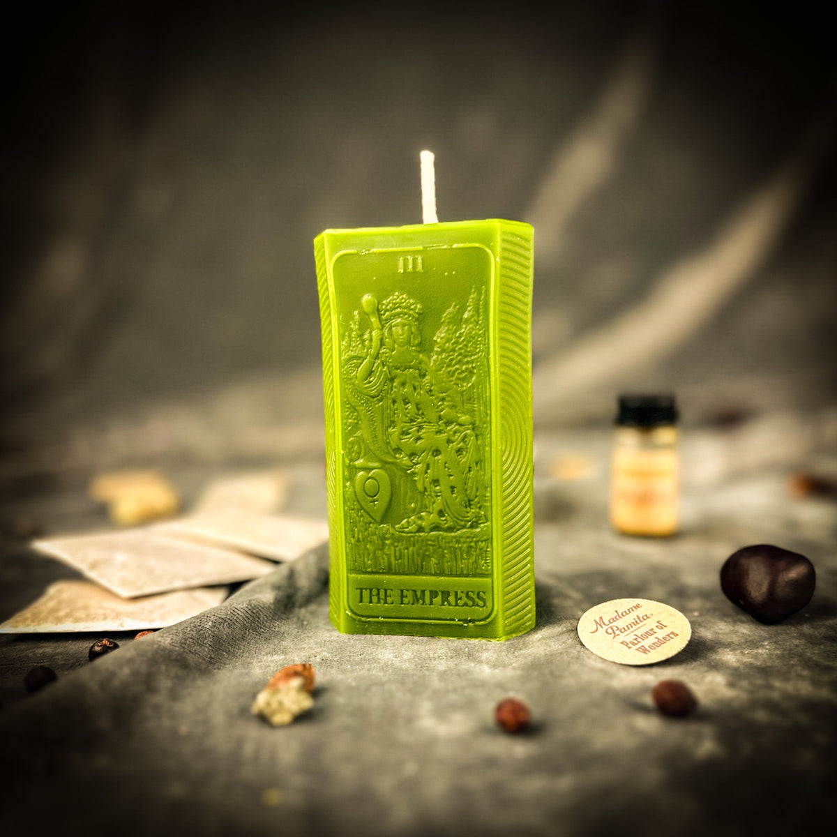 Green beeswax The Empress tarot card candle on gray cloth with a vial of dressing oil and scattered herbs