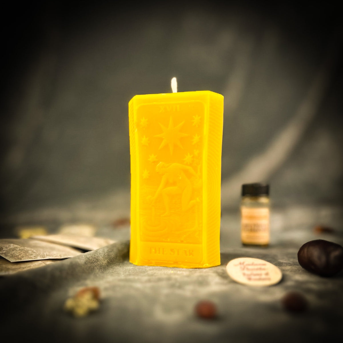 Yellow beeswax candle molded as The Star tarot card, standing upright beside a small vial of dressing oil