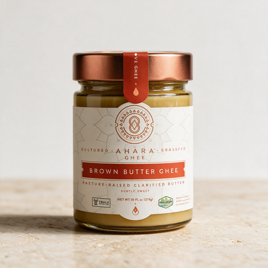 Glass jar of Ahara Cultured Grassfed Brown Butter Ghee with a copper lid, standing on a pale stone counter