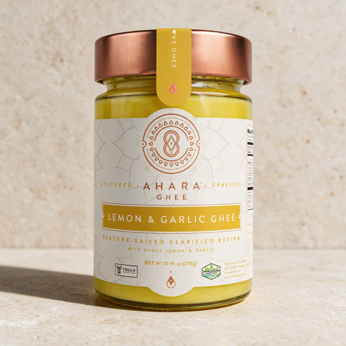 Ahara Rasa Lemon and Garlic ghee in the 10 fl oz jar with a copper lid and yellow label on pale stone